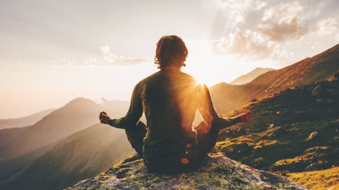 Man mediterar på berg i solnedgången